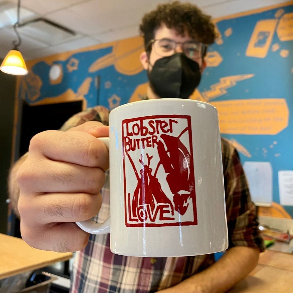 Barista Jeremiah charismatically extends a mug of coffee with the Lobster Butter Love logo towards the camera.