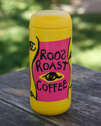 Yellow thermos with pink label featuring 'Rooz Roast Coffee' on a wooden surface with greenery in the background