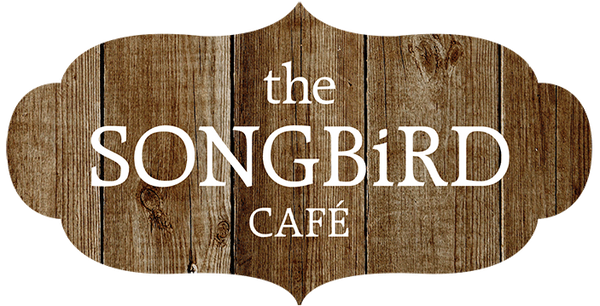 A decorative wooden sign with scalloped edges reading 'the SONGbIRD CAFÉ' in white text on a rustic brown wood plank background, shown on a white backdrop.