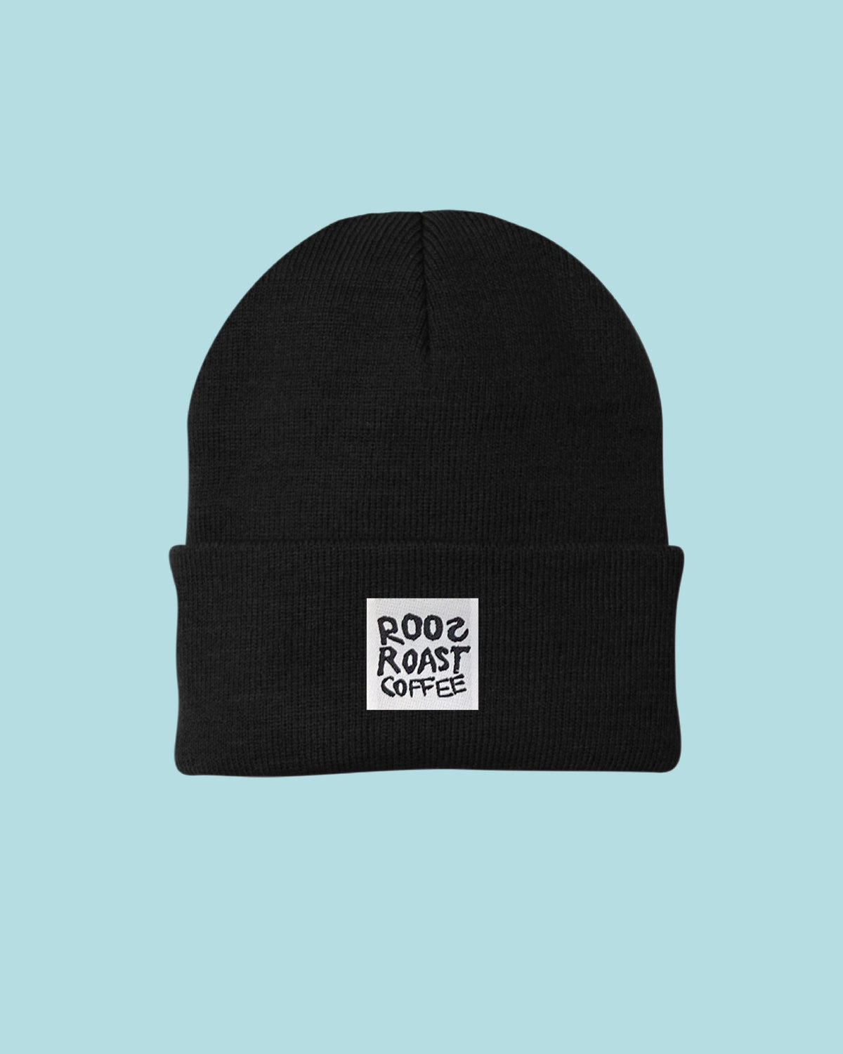 A black knit beanie hat with a white square patch on the front cuff that reads 'ROOsROAST COFFEE' in black text, centered on a light blue background.