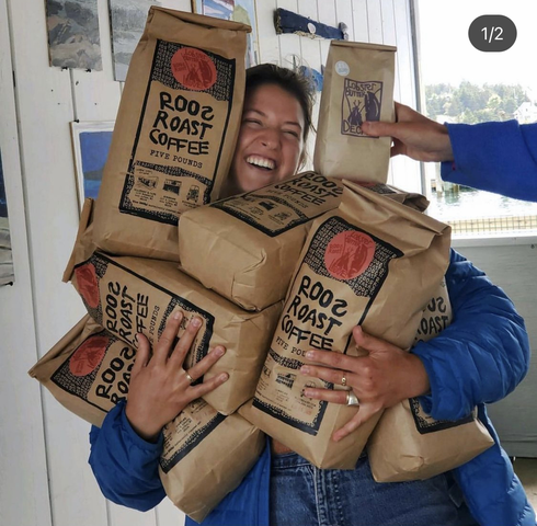 a smiling employee holding as many five pound bags of roosroast coffee as possible