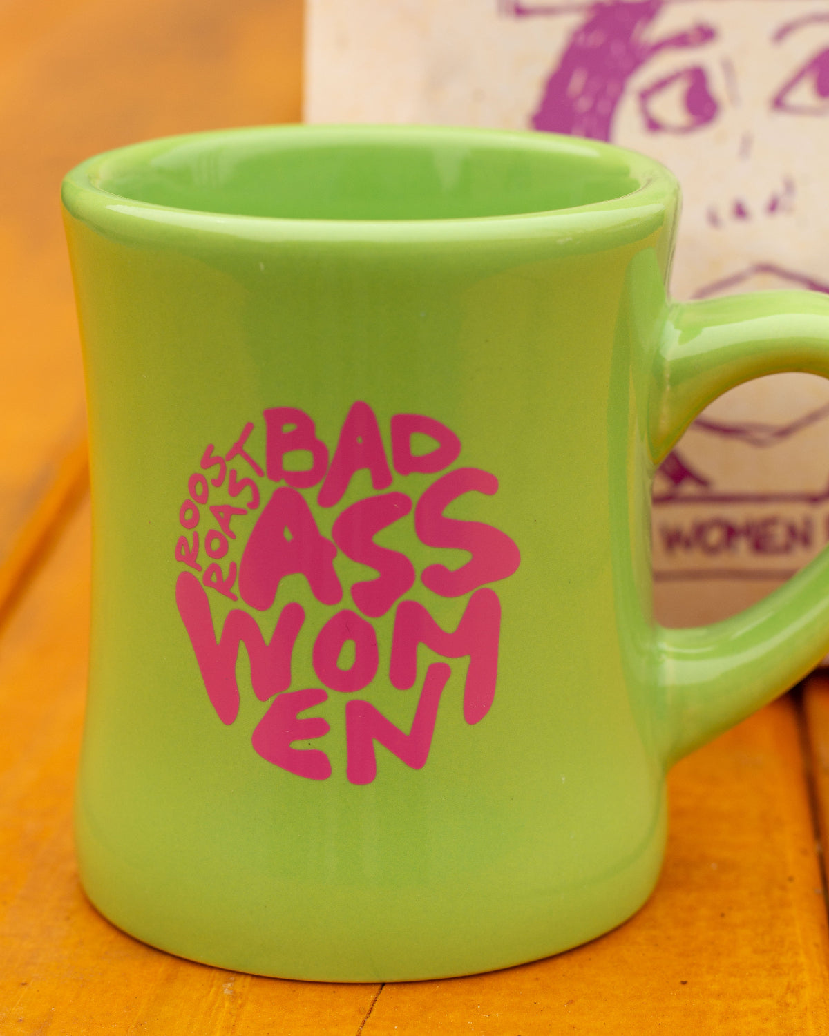Green mug with pink 'Bad Ass Women' text on a wooden surface