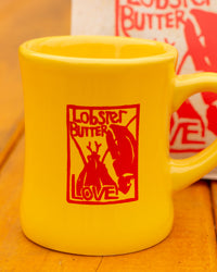 Yellow mug with red 'Lobster Butter Love' design on a wooden surface