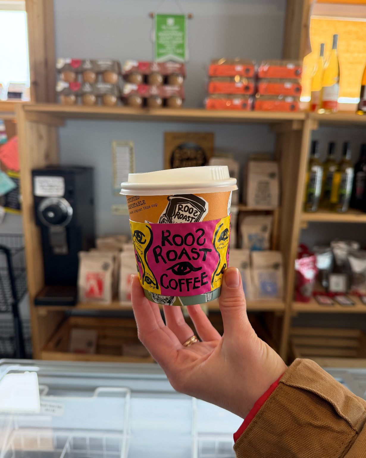Hand holding a coffee cup with a 'Root Roast Coffee' label in a store setting.