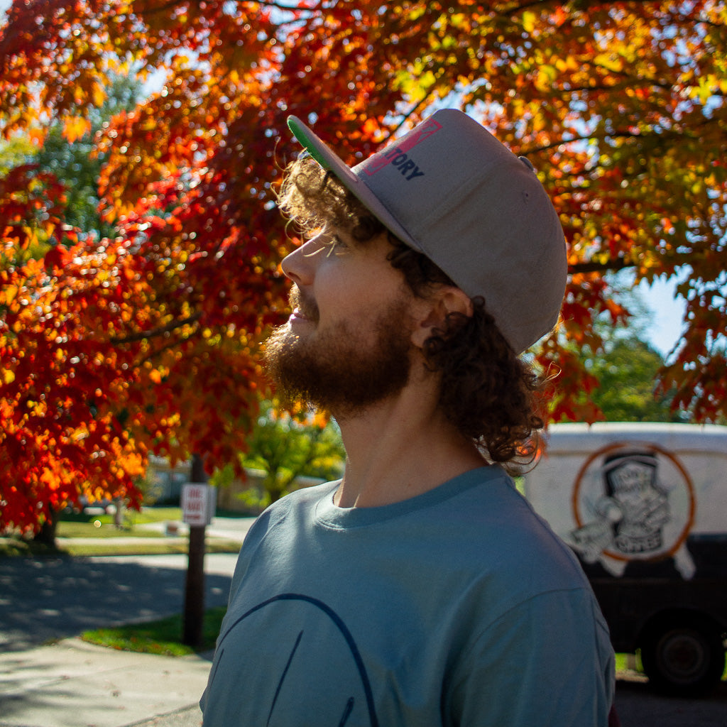 looking up into the trees while wearing gray lobster butter trucker hat