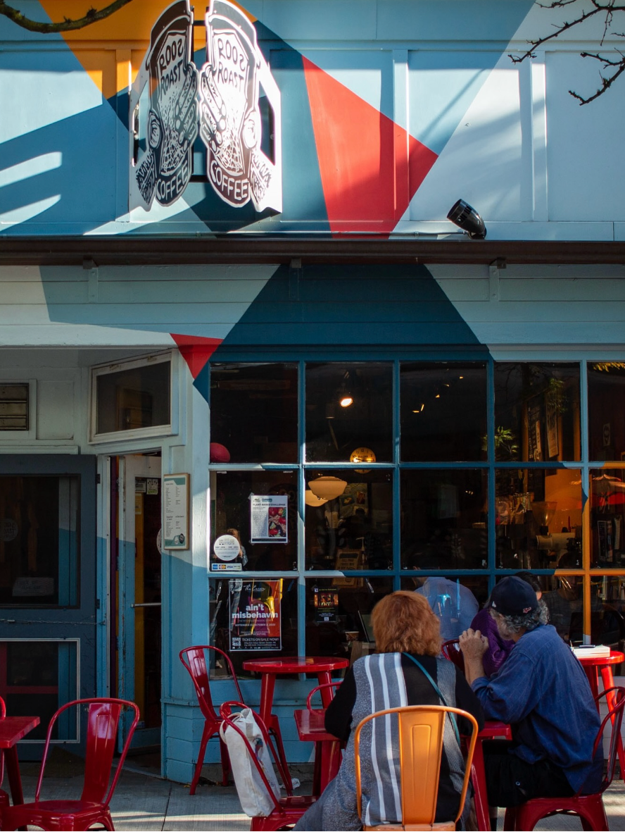 Two people sitting at a table outside a colorful building with a large logo on the wall.