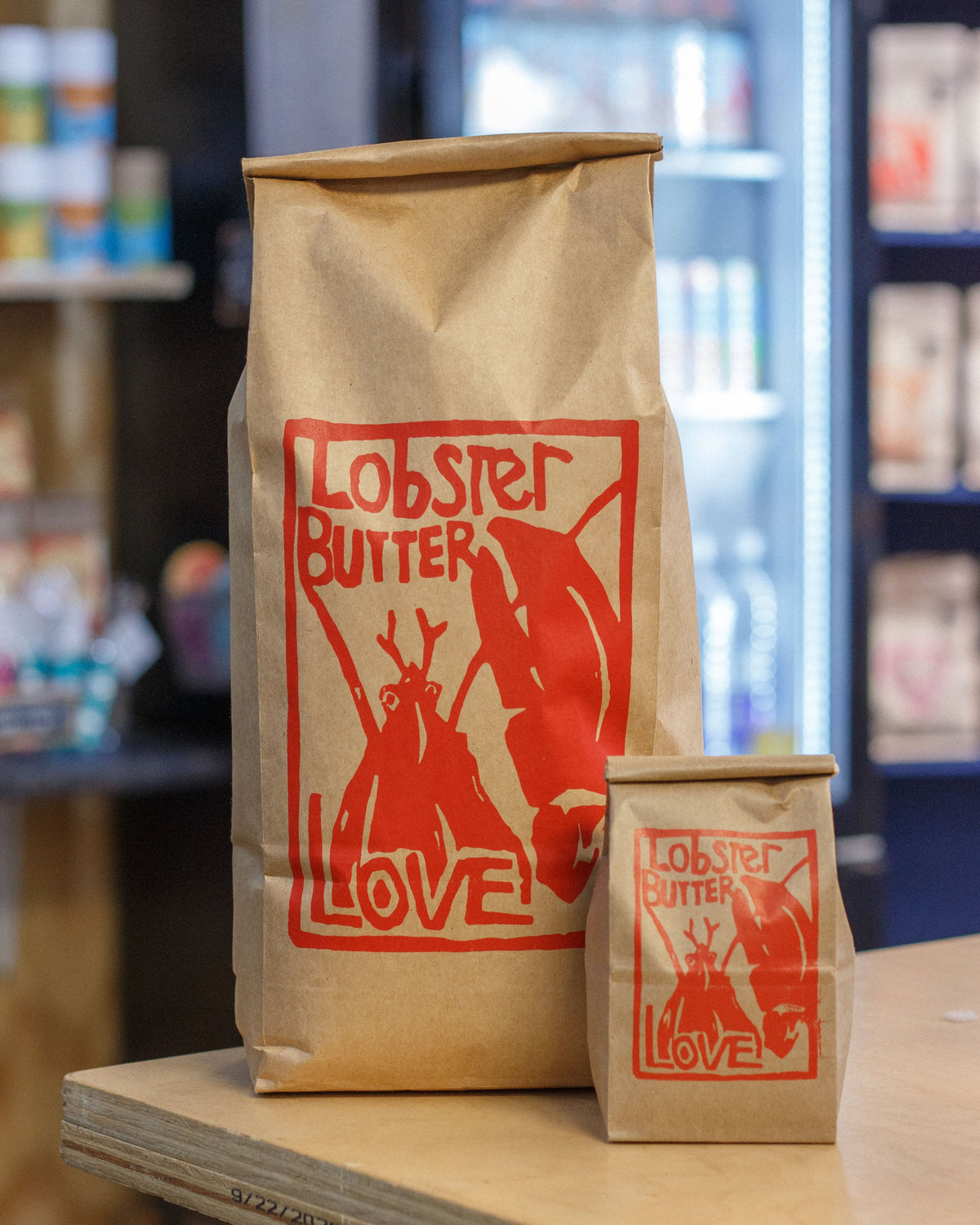Two brown paper bags with red 'Lobster Butter Love' logo on a wooden surface.