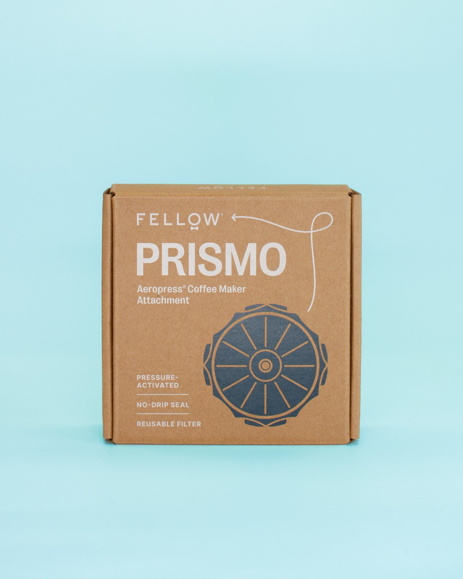 A brown cardboard product box for Fellow Prismo Aerograss Coffee Maker Attachment, featuring white text and a dark blue circular graphic, set against a solid light blue background.