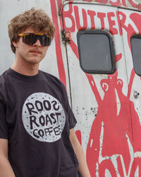 Person wearing a black t-shirt with 'Roos Roast Coffee' logo in front of a vehicle with red graphics.