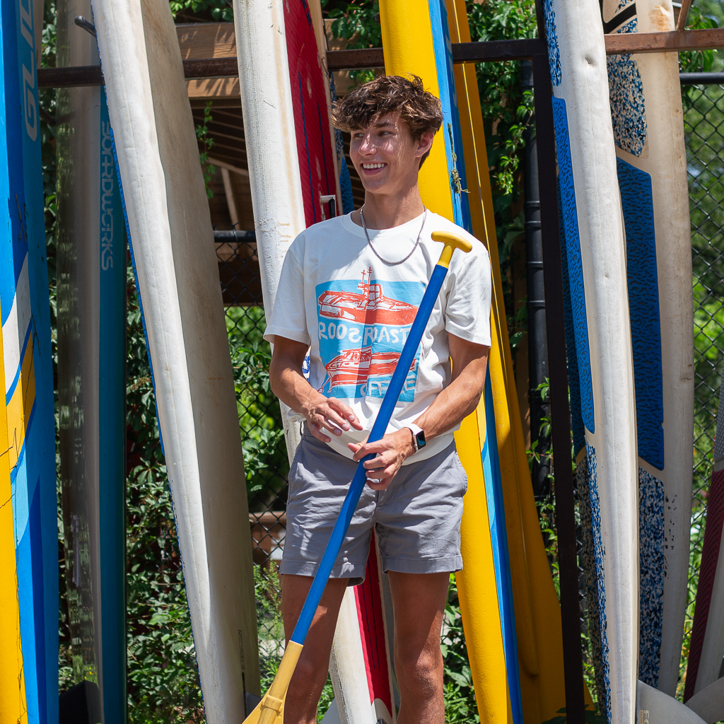kid smiling and holding a paddle while wearing screen printed t-shirt by roosroast coffee