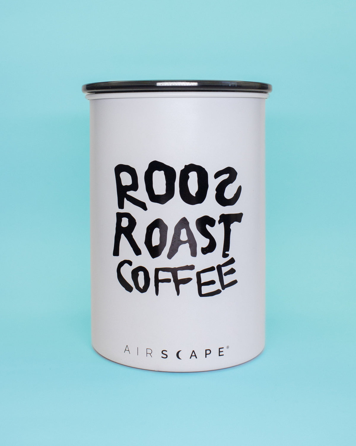 A white cylindrical coffee canister with a black lid, featuring the text 'ROOs ROAST COFFEE' in a black hand-drawn font and 'AIRSCAPE' at the bottom, set against a solid light blue background.